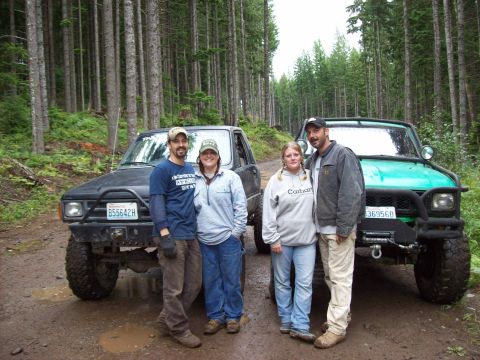 1985 Toyota Pickup/SR5 - Four people pose with two modified 1985 Toyota Pickup SR5 trucks in a forest setting.