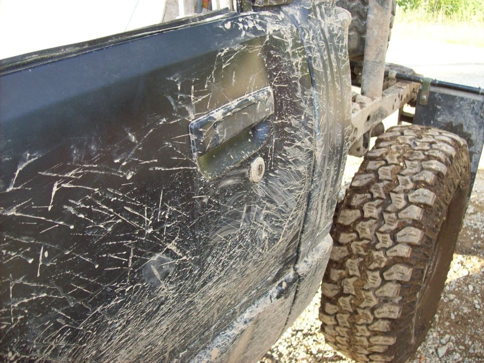 Mud-splattered black 1985 Toyota Pickup SR5 door and off-road tire, side view