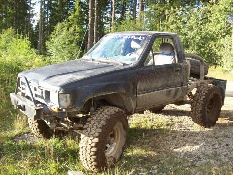 1985 Toyota Pickup/SR5 - This modified 1985 Toyota Pickup features large off-road tires and a custom rear bed setup, seen in a wooded area.