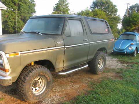 1979 Ford Bronco - A green Ford Bronco and a blue VW Beetle are parked outdoors on a gravelly area.
