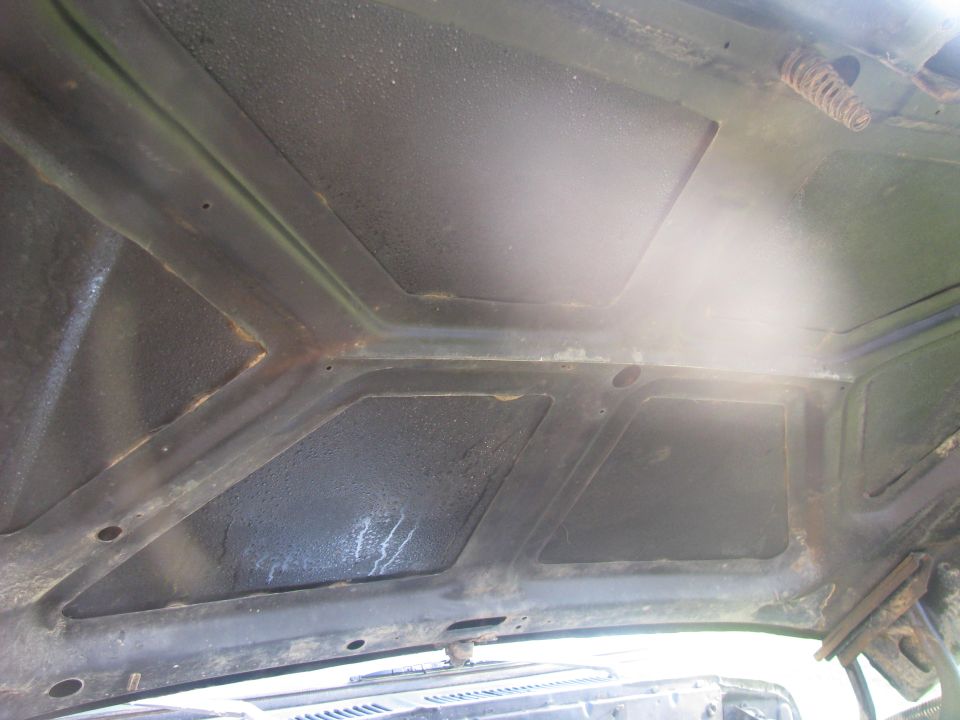 underside of a car hood with visible bracing and a spring