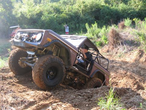 1967 Ford Mustang - A modified Ford Bronco navigates a muddy off-road course, with another vehicle visible in the distance.