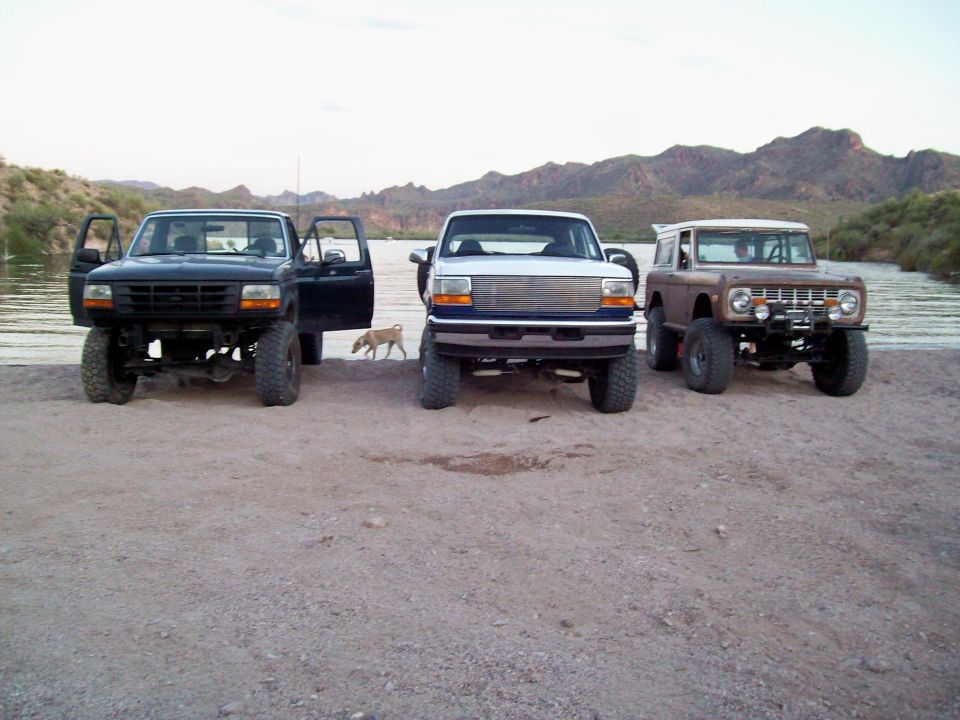 Brown 1978 Ford Bronco with lifted suspension and off-road tires parked by a body of water