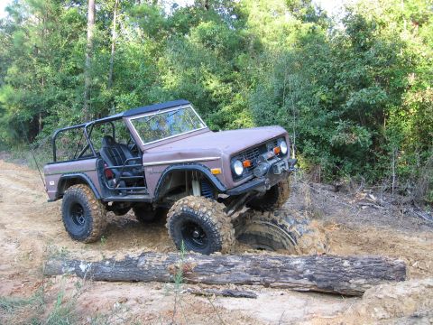 1967 Ford Mustang - A modified Ford Bronco navigates a muddy obstacle course, with one wheel deep in the mire.