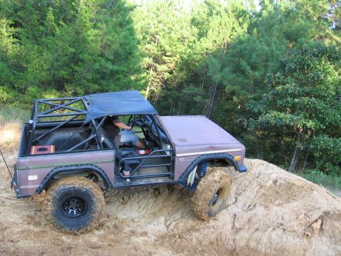 1967 Ford Mustang - A modified off-road vehicle navigates a dirt incline amidst trees.
