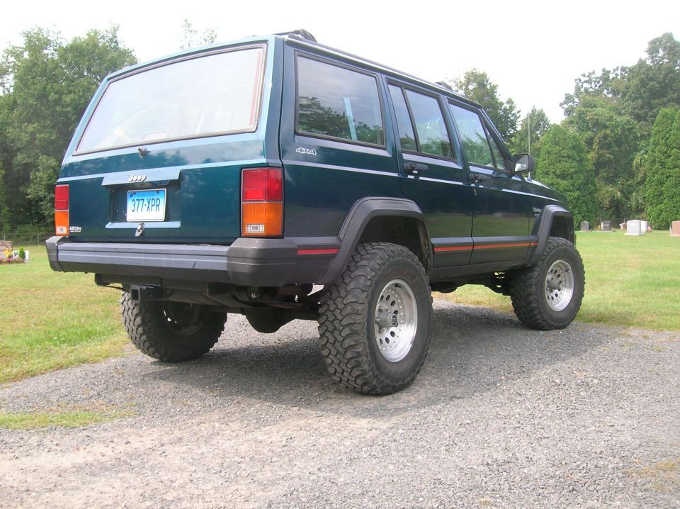 Jeep Cherokee XJ parked on gravel, rear view. Has 377 XPR license plate and 4x4 decal