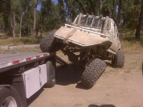 1992 Ford F-350 - A heavily modified pickup truck is loaded onto a flatbed trailer in a wooded area.