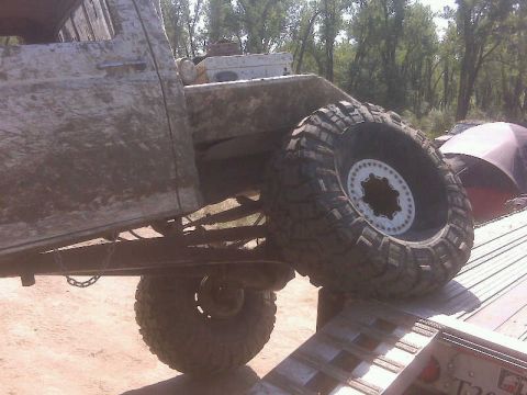1992 Ford F-350 - A heavily mud-splattered truck bed and a large off-road tire are visible as the vehicle is loaded onto a trailer.