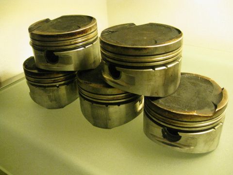 1994 Ford Probe - Several engine pistons are stacked on a reflective surface, showing signs of wear.
