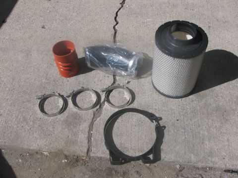 1996 Ford C-350 (Centurion Conversions) - A TYMAR Open air Intake kit is laid out on a concrete surface, including a cylindrical air filter, a flexible hose, and several metal clamp…