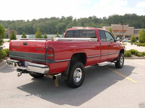 1989 Ford Bronco - Rear three-quarter view of a red Dodge Ram extended-cab long-bed 4x4 pickup parked in a shopping center lot in front of a Hobby Lobby, with…