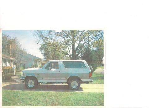 1994 Ford Bronco - This Ford Bronco is parked on a residential street with a tree and houses in the background.
