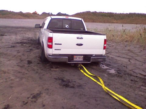 1998 Dodge 1500 - White Ford F-150 is stuck in mud, with a yellow tow strap attached to the rear bumper.