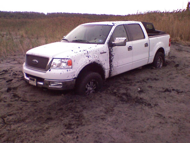 White Ford F-150 stuck in mud, front passenger side wheel deep