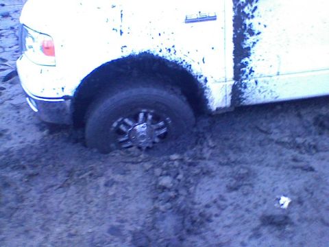 1998 Dodge 1500 - A white pickup truck is stuck in thick mud, with its front wheel submerged.