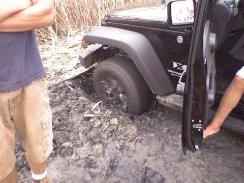 1998 Dodge 1500 - A Jeep Wrangler is stuck in thick mud, with its front wheel submerged and the driver's door open.