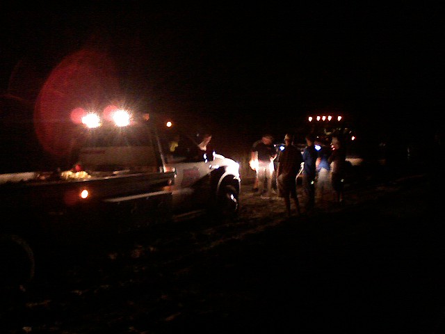 Truck with auxiliary lights on, side view at night, with people standing nearby