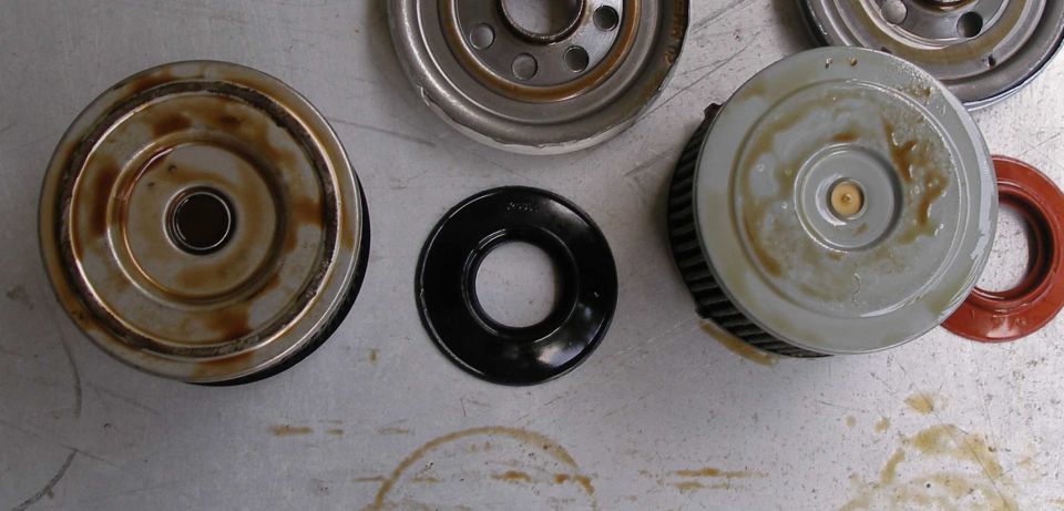 Bottom view of two oil filters and rubber sealing gaskets on a stained metal bench