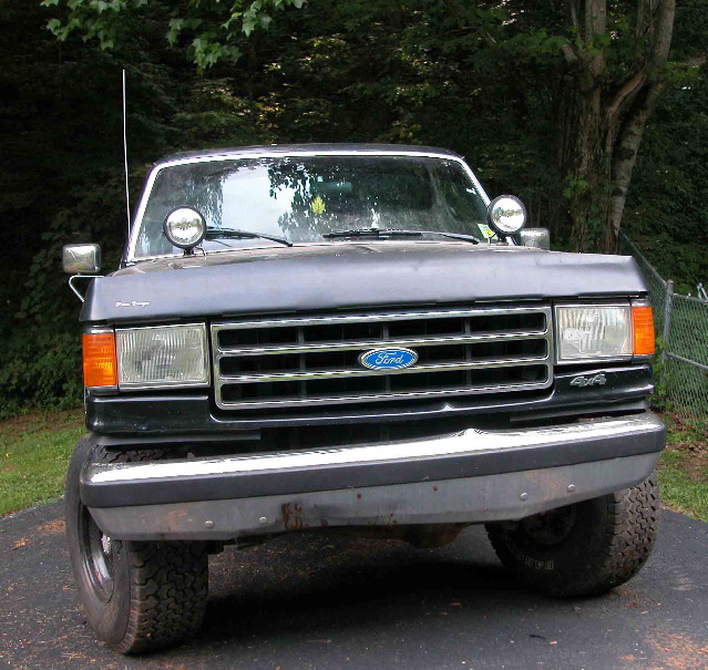 Front end of black lifted Ford truck with auxiliary lights, antennas and Ford grille
