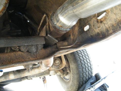 1982 Ford Bronco - Close-up view of the underside of a vehicle, focusing on a welded exhaust pipe and rusty frame components.