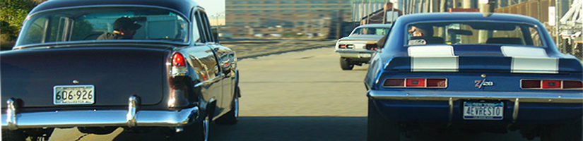 Panoramic crop of a 1950s sedan and a blue Camaro Z/28 shot from behind on a street