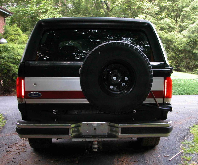 Rear of black Ford Bronco with tailgate-mounted spare tire and red striping