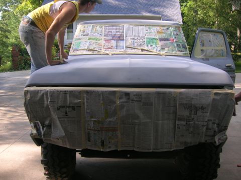1975 Ford F-250 - A person sands the hood of a 1975 Ford F-250 truck, which is covered in newspaper for protection during preparation for painting.