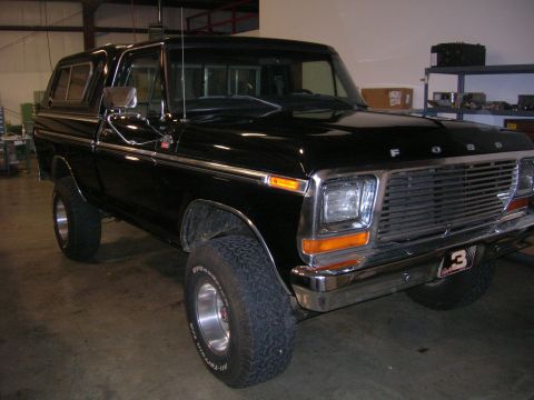 1975 Ford F-250 - This black Ford pickup truck is shown from the front-right side, a camper shell and chrome accents.