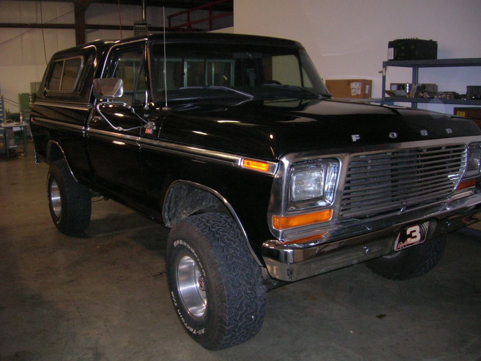 Black Ford pickup truck with camper shell, front quarter view. Has a chrome grille and bumper