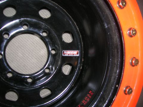 1975 Ford F-250 - Close-up of a black truck wheel with an orange outer rim, showing a MRW brand sticker.