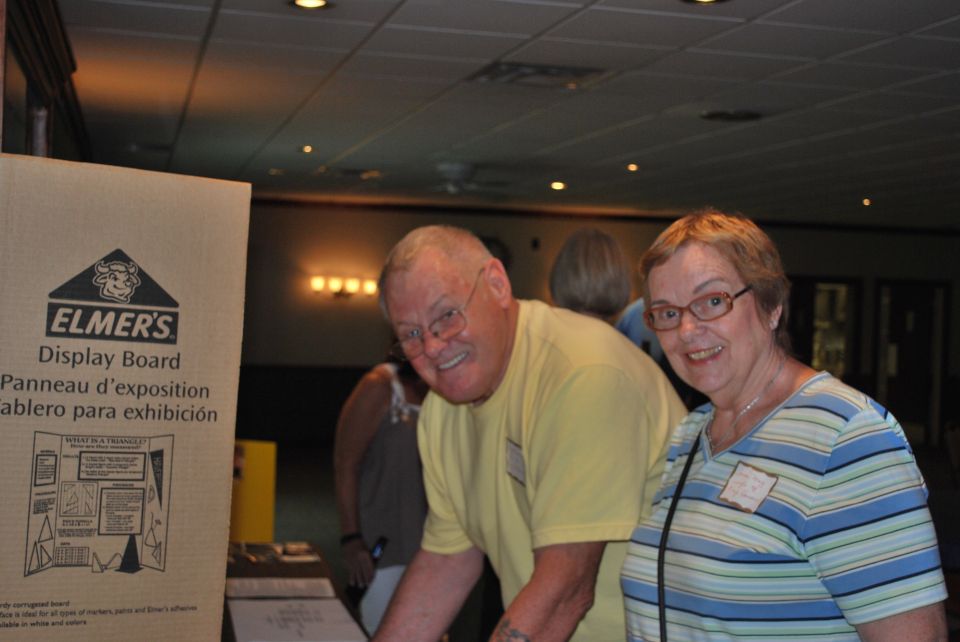 Cardboard display board with Elmer's logo and text, two people smiling