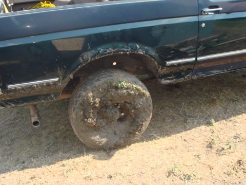 1992 Ford Bronco - Mud-caked rear tire and fender of a dark green 1992 Ford Bronco.