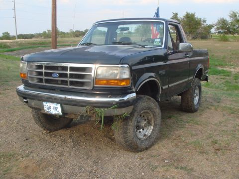 1992 Ford Bronco - A dark green 1992 Ford Bronco with a lifted suspension sits on a dirt lot under a cloudy sky.