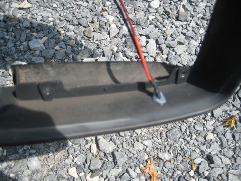 1993 Ford Probe - A close-up shows a black plastic automotive trim piece with a red wire attached, resting on a bed of gravel.