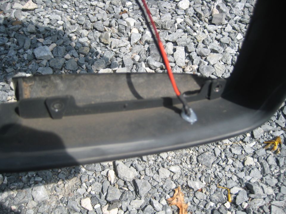 close-up of black plastic trim with red wire attached, sitting on gravel