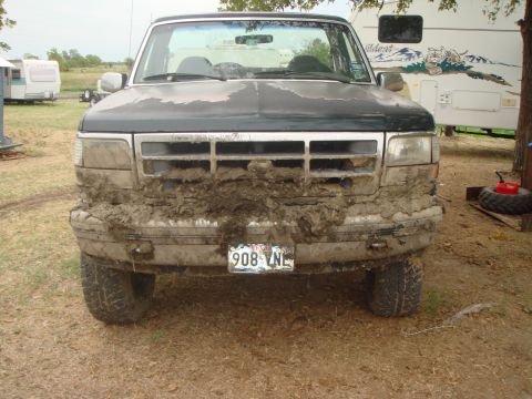 1992 Ford Bronco - A muddy 1992 Ford Bronco is parked outdoors, with a trailer visible in the background.