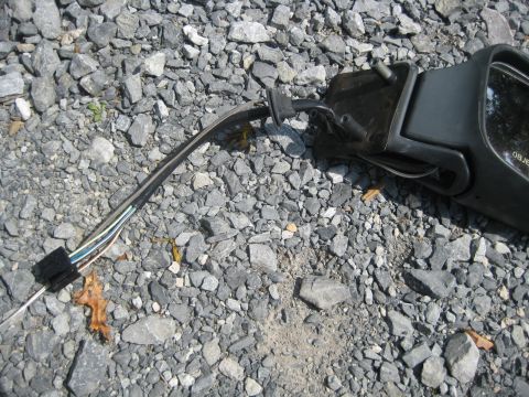 1993 Ford Probe - Side mirror assembly with wiring detached, resting on a gravel surface.