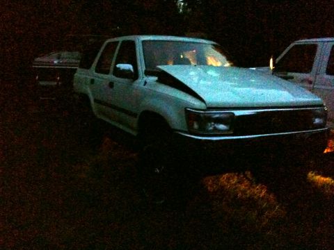 1993 Toyota 4Runner - A light-colored SUV sits in a dark outdoor setting with its hood damaged and propped open.
