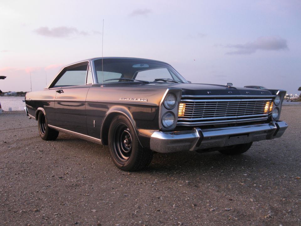 Dark blue Ford Galaxie 500 hardtop at sunset on gravel, parking lamps lit, black steel wheels