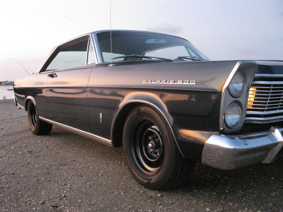 Low front-quarter view of dark blue Galaxie 500 hardtop on gravel with stacked headlights and steel wheels
