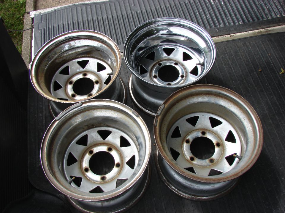 Four steel wheels with triangular cutouts, some showing rust, resting on a truck bed