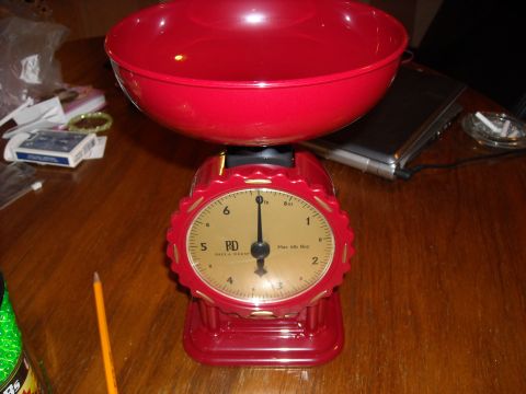 1979 Ford F-150 - A red kitchen scale with a large red bowl sits on a wooden table, with a pencil nearby.