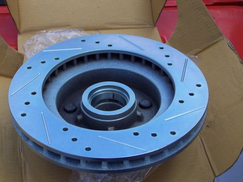 1973 Ford Ranchero - A new cross-drilled and slotted vented brake rotor with an integral hub, sitting in its open cardboard box on a red painted surface. The ma…