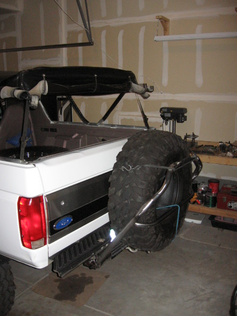 1995 Ford Bronco - The rear of a white Ford Bronco is shown with a spare tire mounted on a custom carrier in a garage setting.