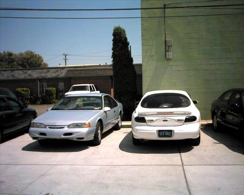 1990 Ford Taurus - A silver Ford Thunderbird is parked in a lot next to a white Ford Taurus.