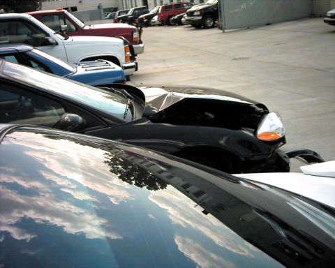 1990 Ford Taurus - A black car's hood is severely damaged, reflecting the sky and surrounding buildings.