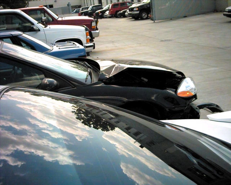black car's hood is crumpled, parked next to other vehicles