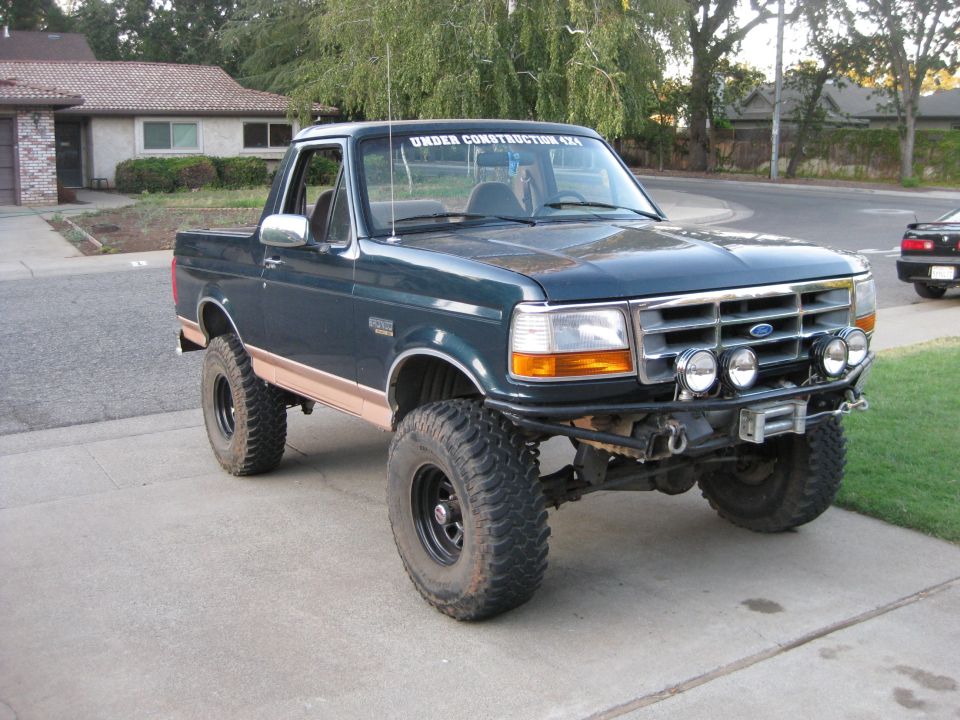 Dark green Ford Bronco with tan trim, lifted with large tires, aftermarket bumper, and winch