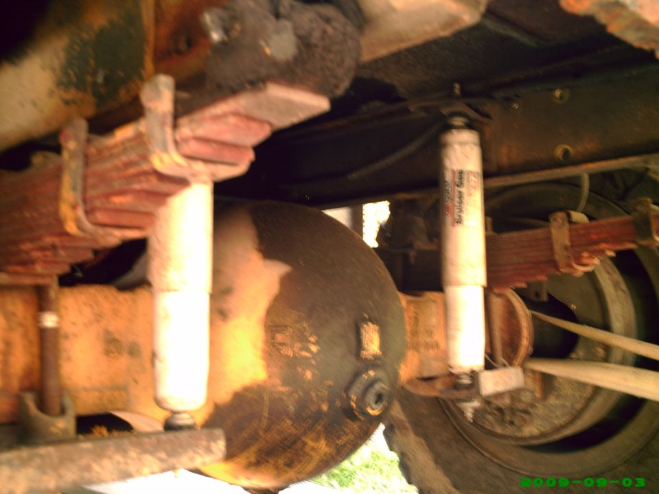 Underside of vehicle showing rusty rear axle, leaf springs, and shock absorbers