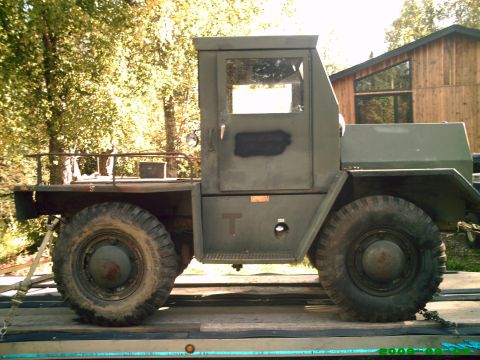 1978 Ford Bronco - Side view of an olive drab military truck with large tires, parked on a trailer.